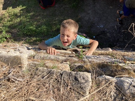 Ein Junge klettert eine mit Sandsteinen aufgesetzte Mauer nach oben. Von oben fotografiert.